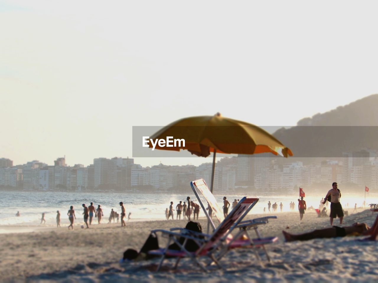 Tilt-shift image of people enjoying at beach against clear sky on sunny day