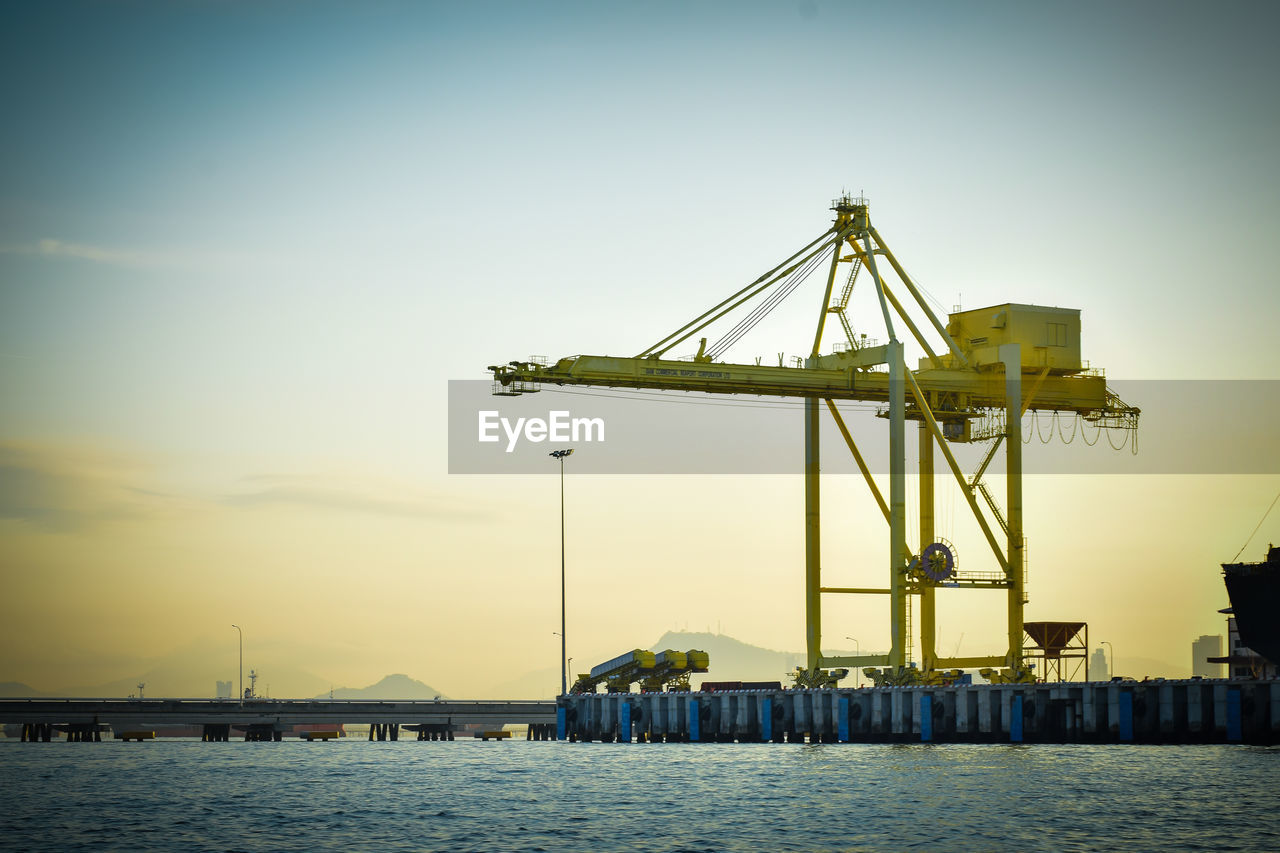 Cranes at commercial dock against sky during sunset