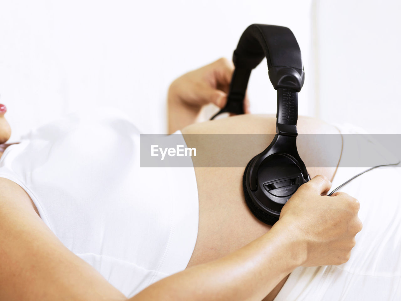 Pregnant woman wearing headphones on belly at home