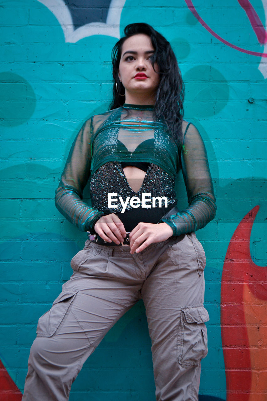 PORTRAIT OF BEAUTIFUL YOUNG WOMAN STANDING AGAINST WALL