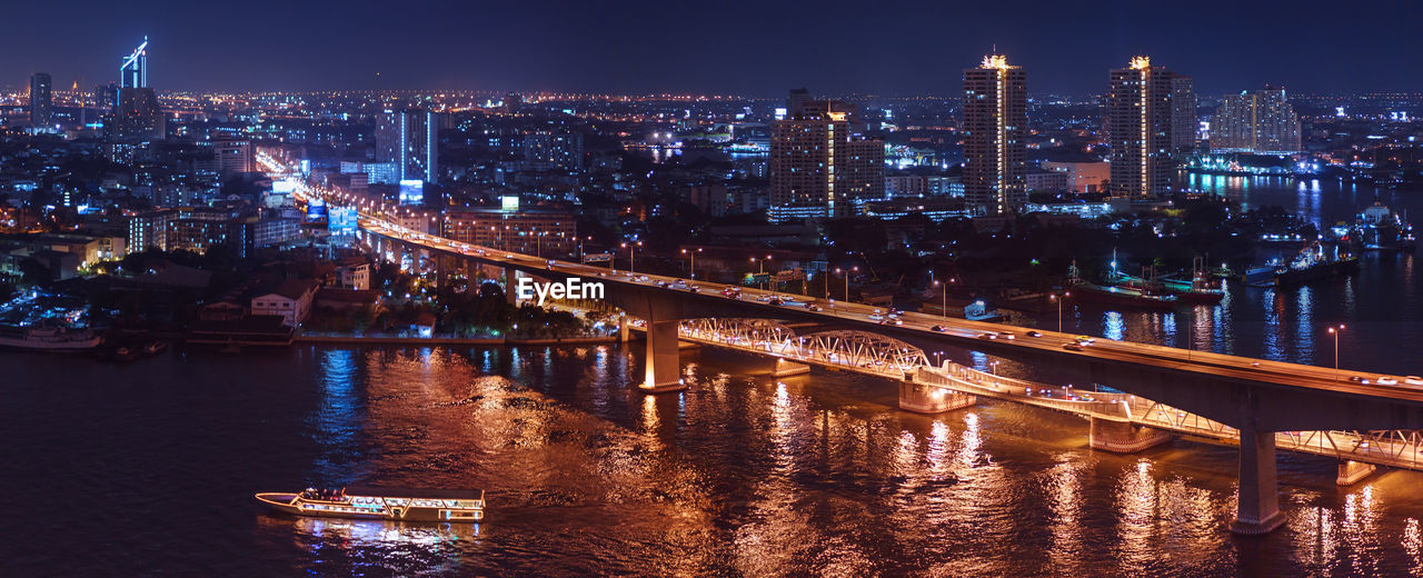 Illuminated bridge over river by buildings in city at night