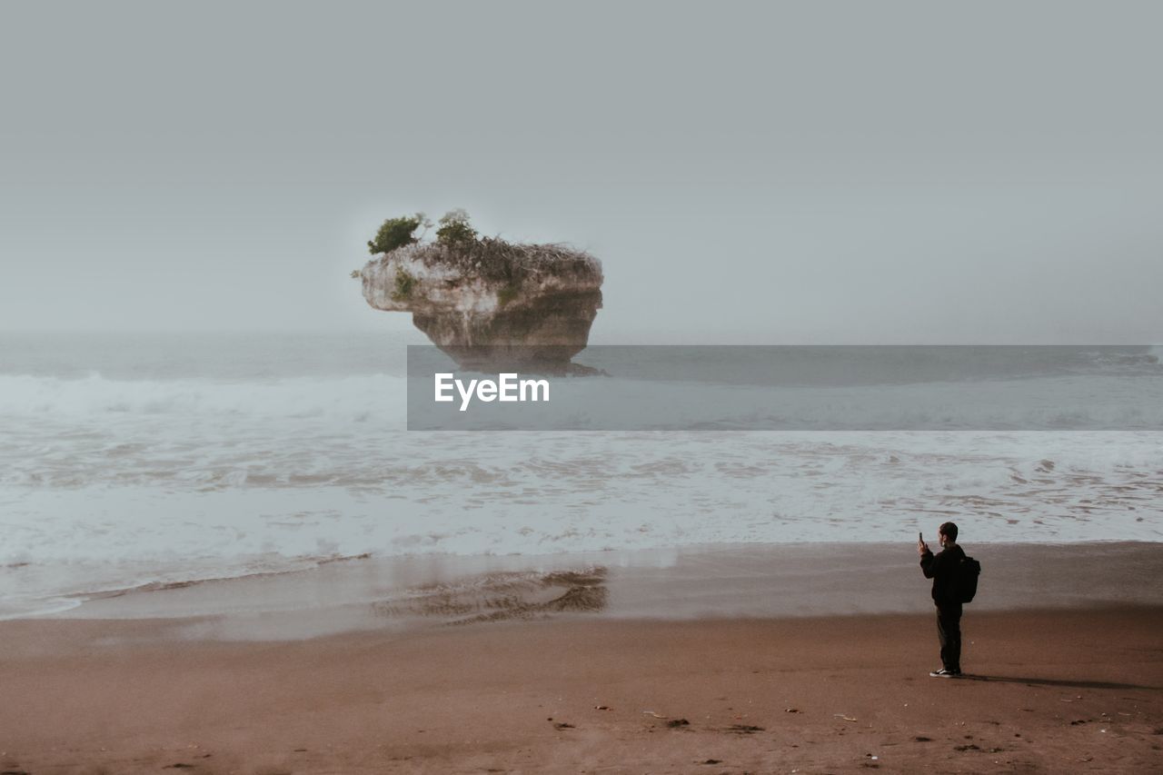 Rear view of woman walking at beach against clear sky