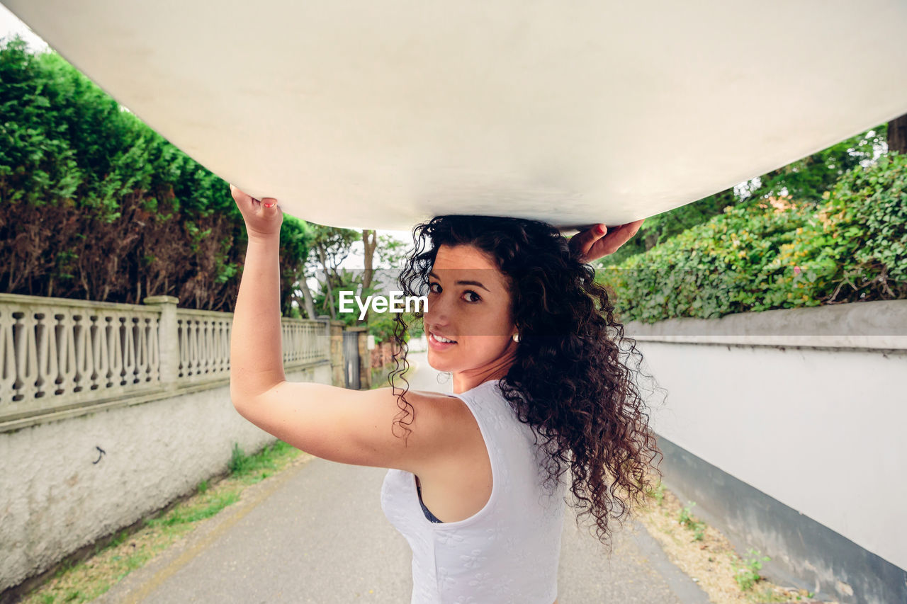 Portrait of young woman carrying surfboard on road