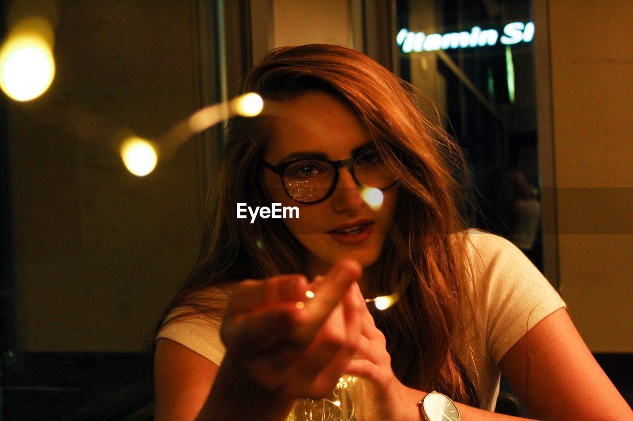 Portrait of young woman gesturing in illuminated restaurant