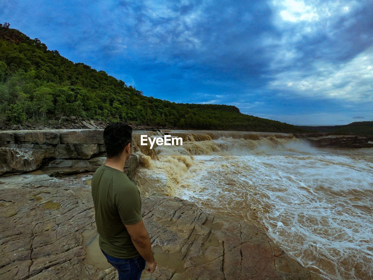 REAR VIEW OF MAN STANDING BY MOUNTAIN AGAINST SKY