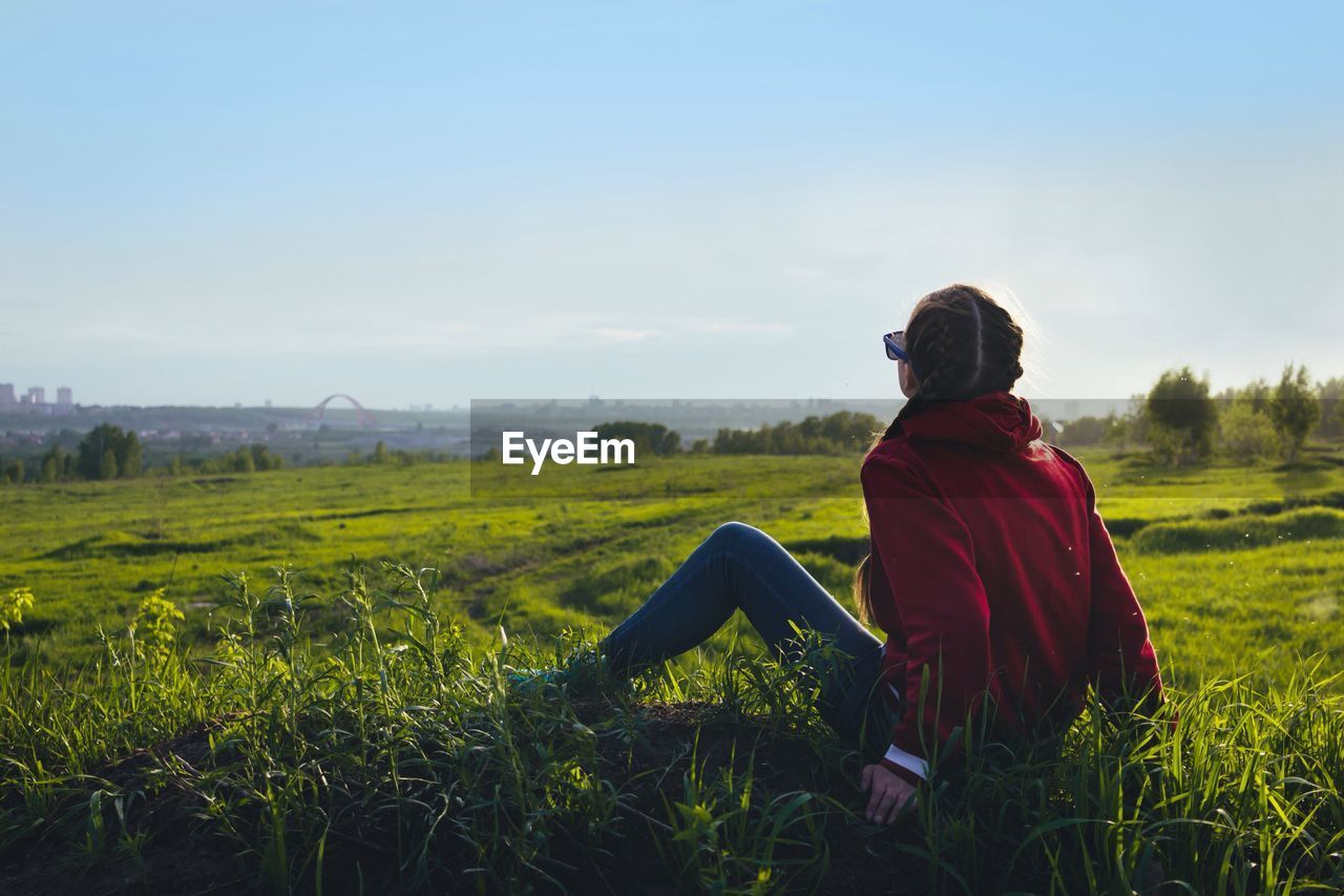 Woman sitting on field against clear sky