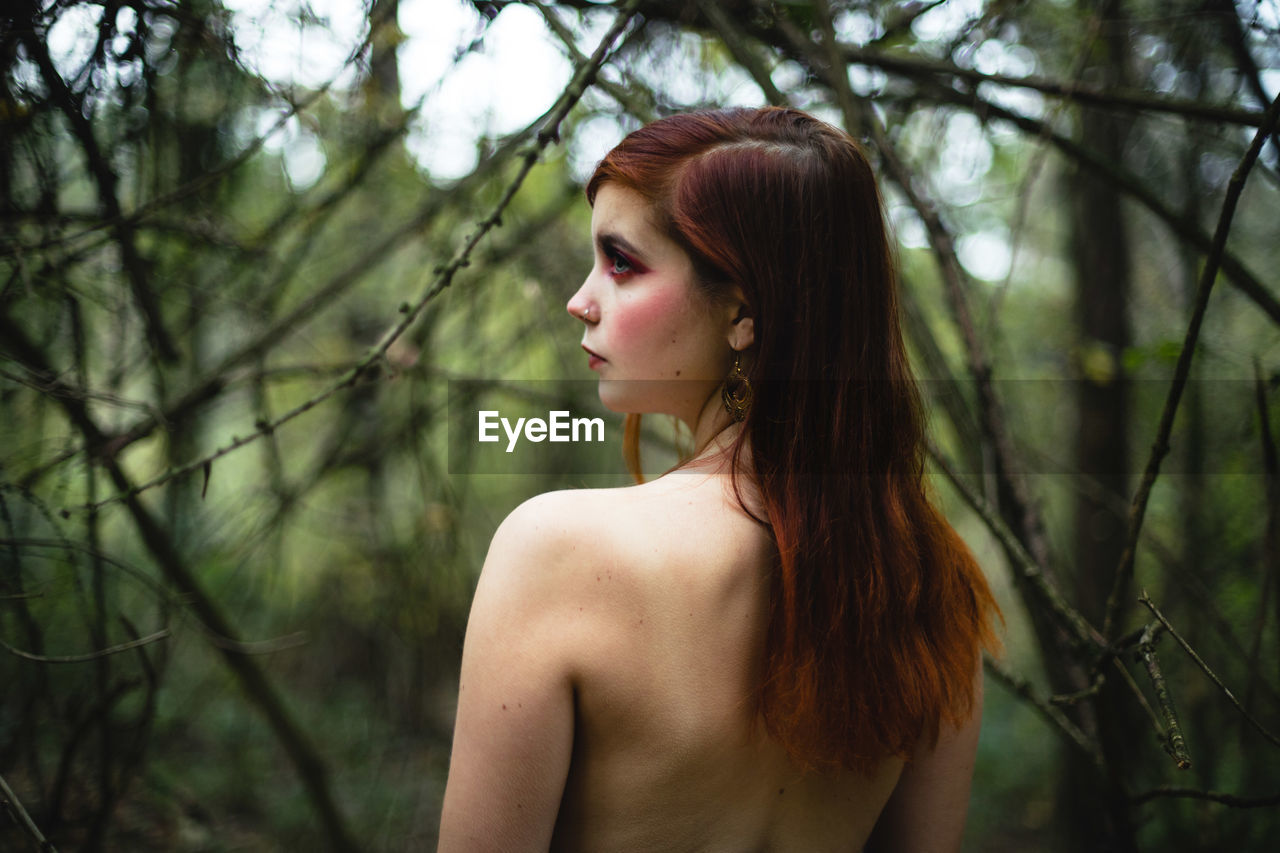 Rear view of topless woman standing in forest
