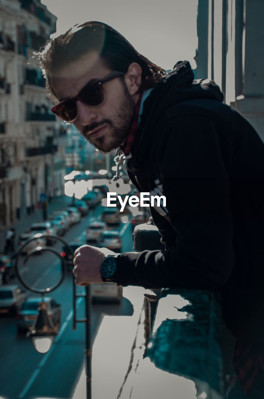 Side view of young man wearing sunglasses standing by railing in balcony