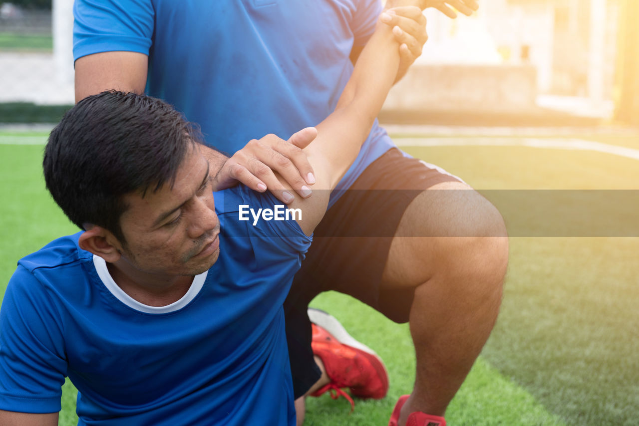 Low section of male physical therapist stretching soccer player hand on field