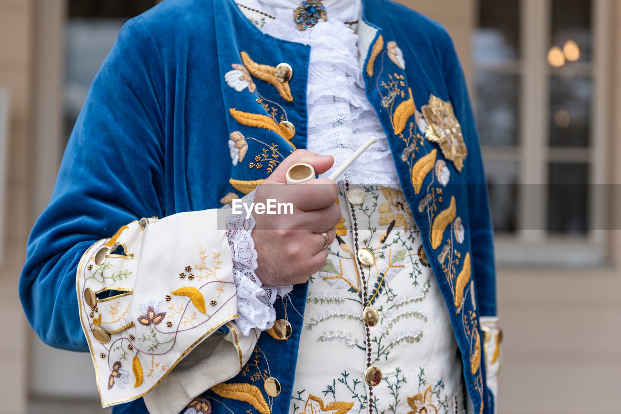 The details of man dressed in a baroque costume. a hand holding a pipe, golden buttons, vest.