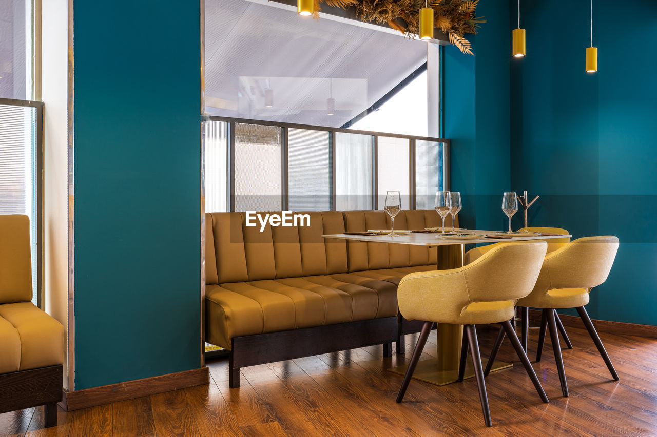 Sofa and comfortable armchairs at table with wineglasses and plates prepared for guests of stylish restaurant