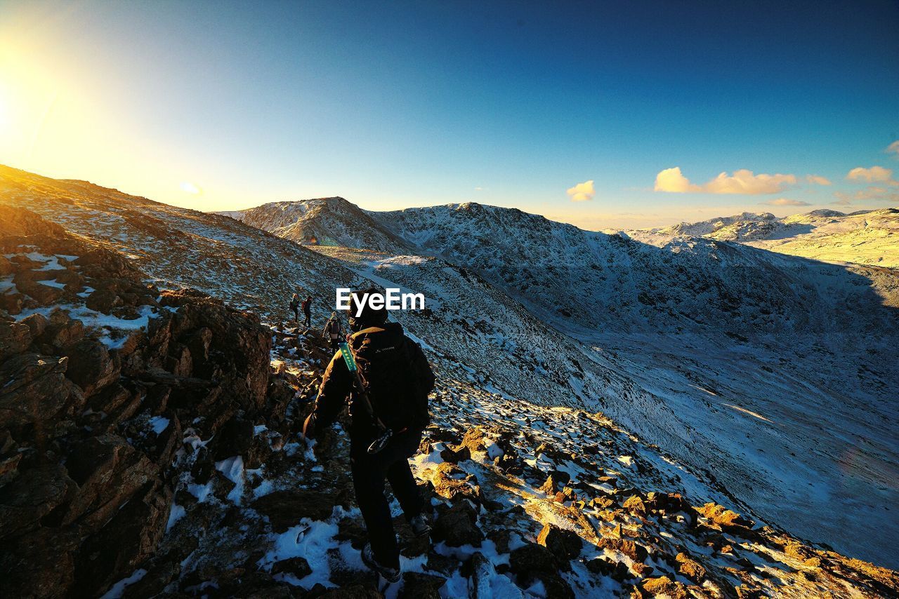 Full length rear view of man standing on snow covered mountains against sky