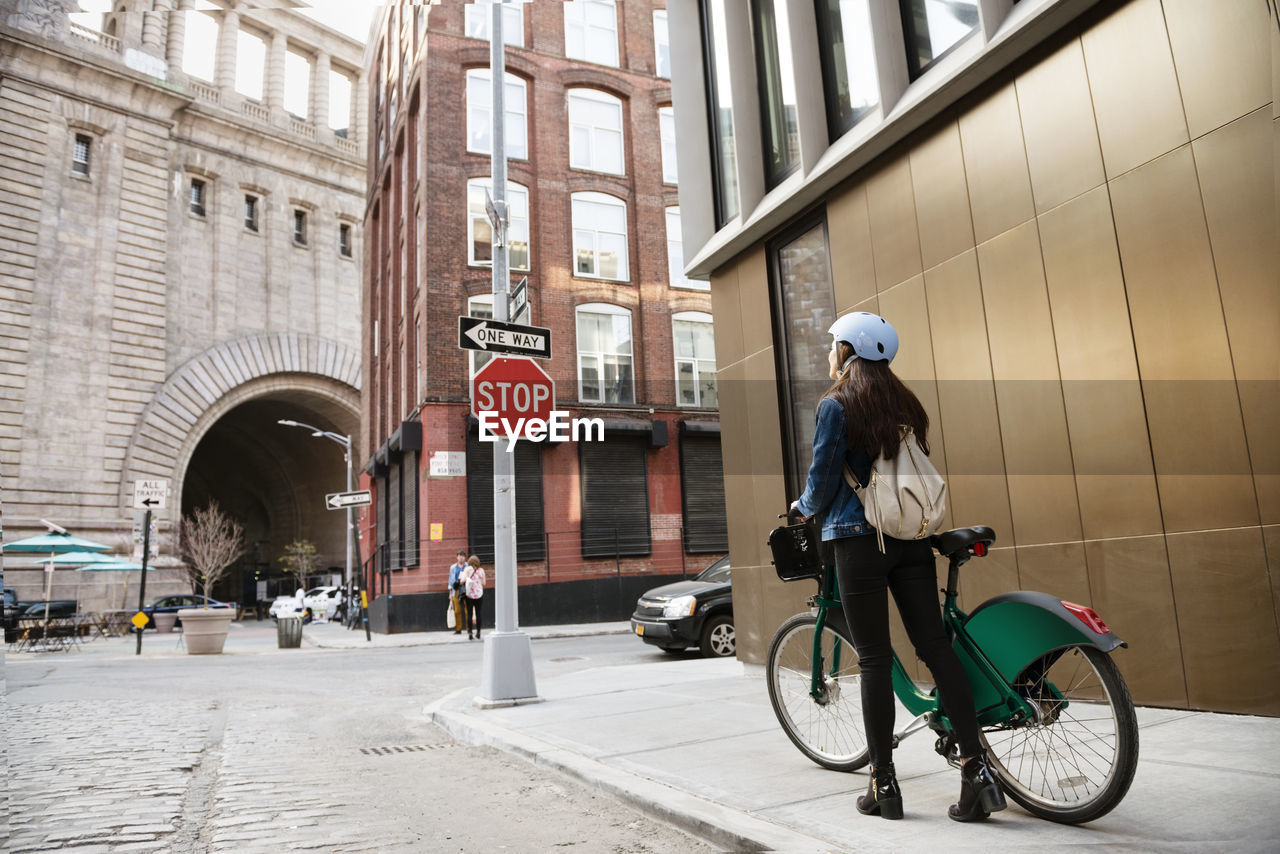 Woman walking with bicycle on sidewalk by building in city