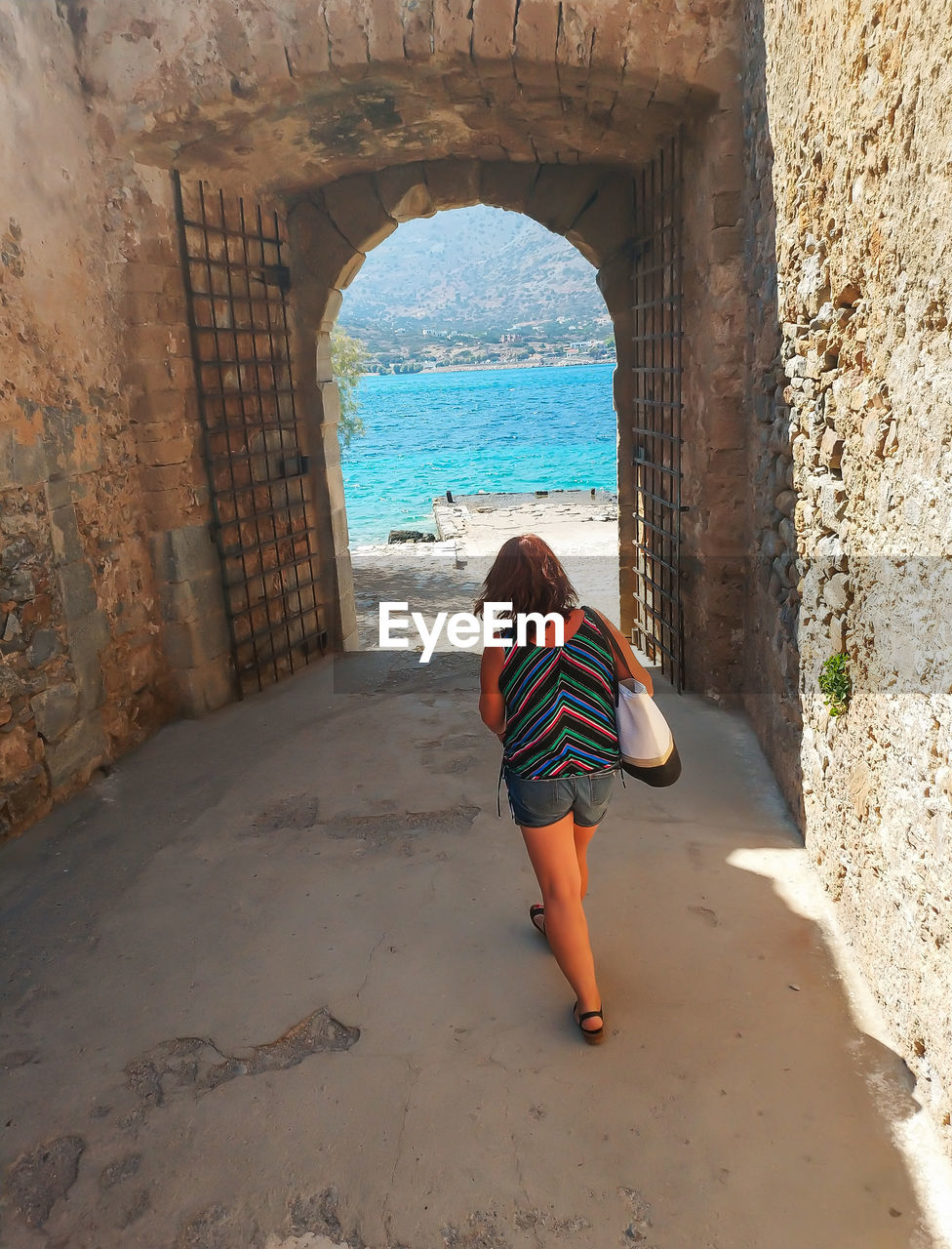 Woman walking under arch discovering fortress spinalonga, greece.