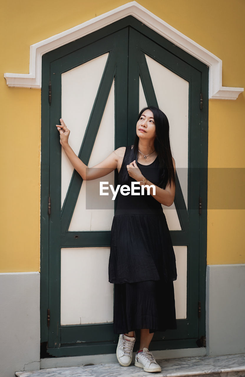 one person, women, adult, full length, standing, black, dress, portrait, young adult, architecture, fashion, female, door, indoors, lifestyles, clothing, entrance, front view, smiling, looking at camera, hairstyle, emotion, long hair, building, photo shoot, looking