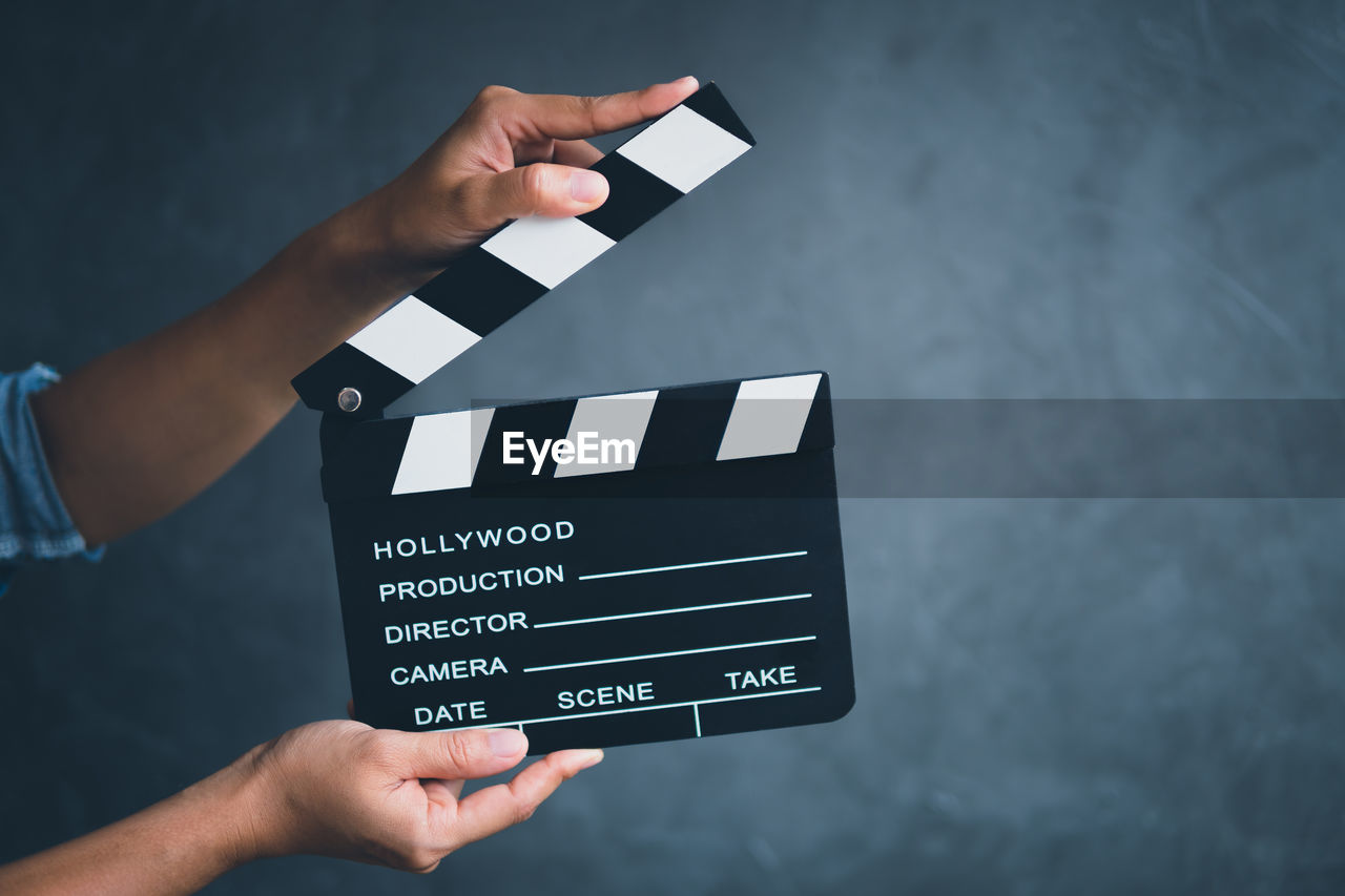 Cropped hands of person holding film slate with text against black background