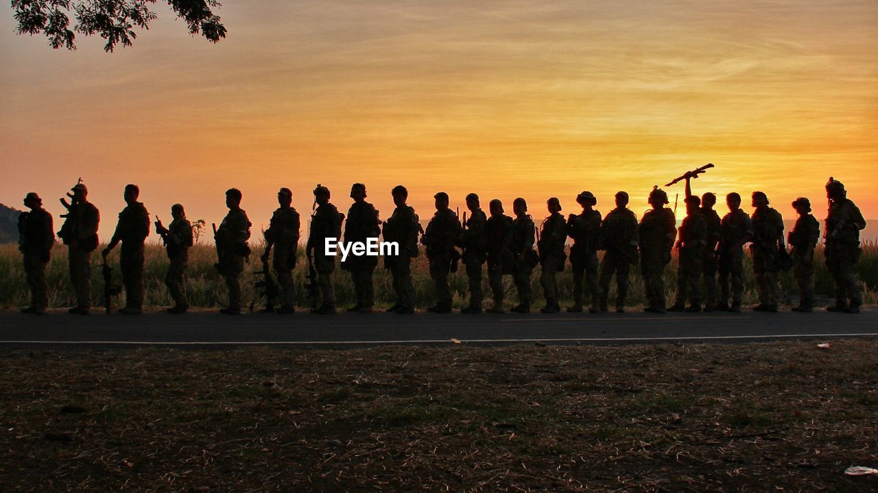 Army soldiers standing on road against sky during sunset