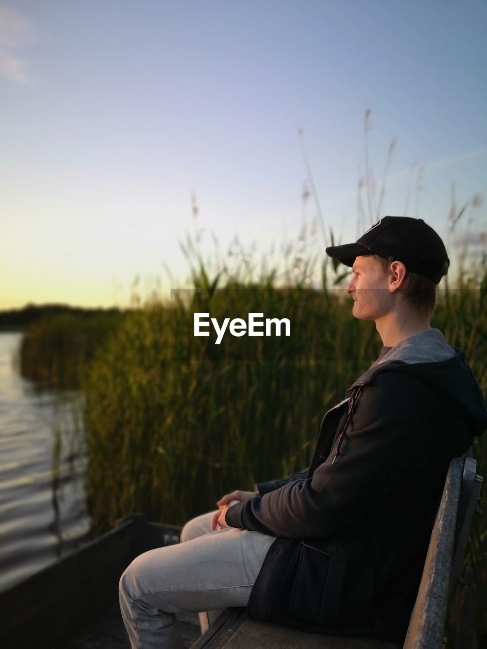 SIDE VIEW OF YOUNG MAN LOOKING AWAY AGAINST LAKE