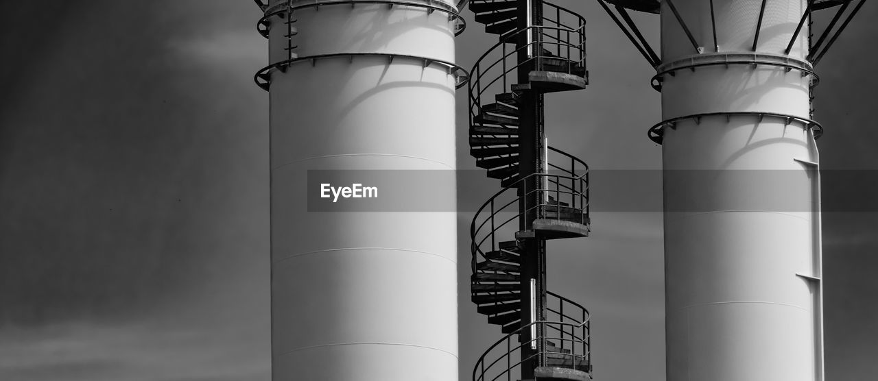 Section of a metal spiral staircase on an industrial building with two chimneys in black and white