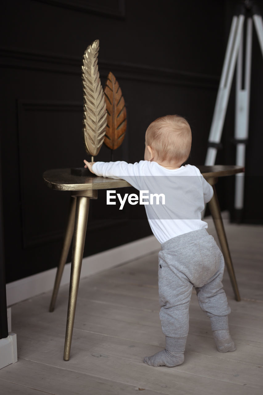 Baby stands at support and reaches out to things on the table, concept of child development 