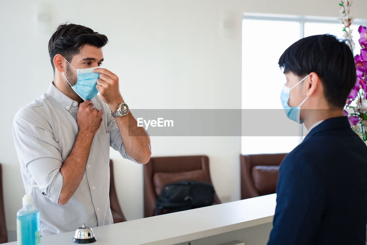 Young man wearing mask standing at hotel reception