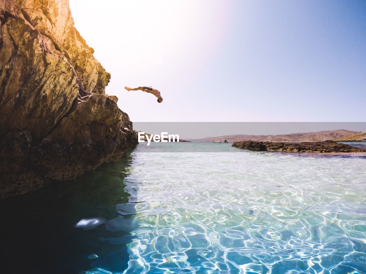 Man diving into sea from cliff against clear sky