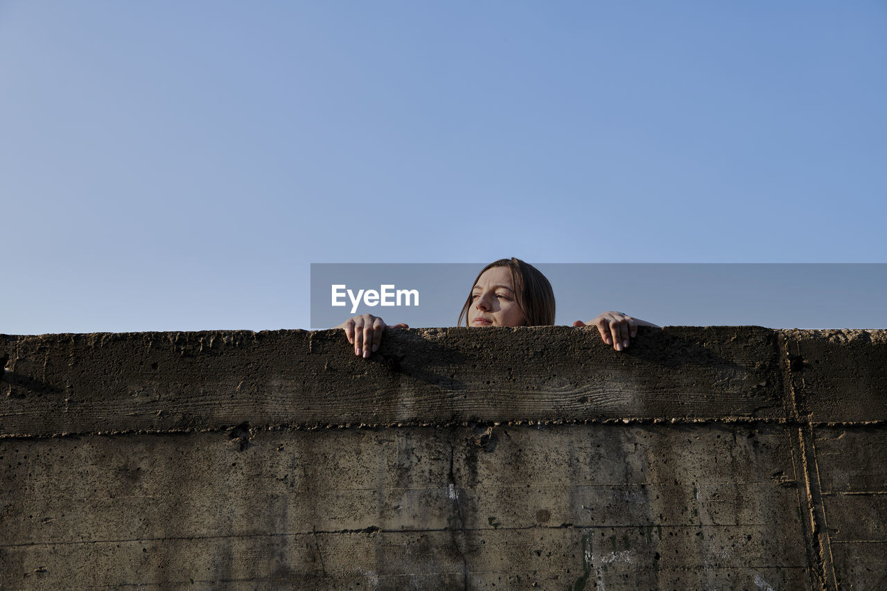 Young woman looking over concrete wall