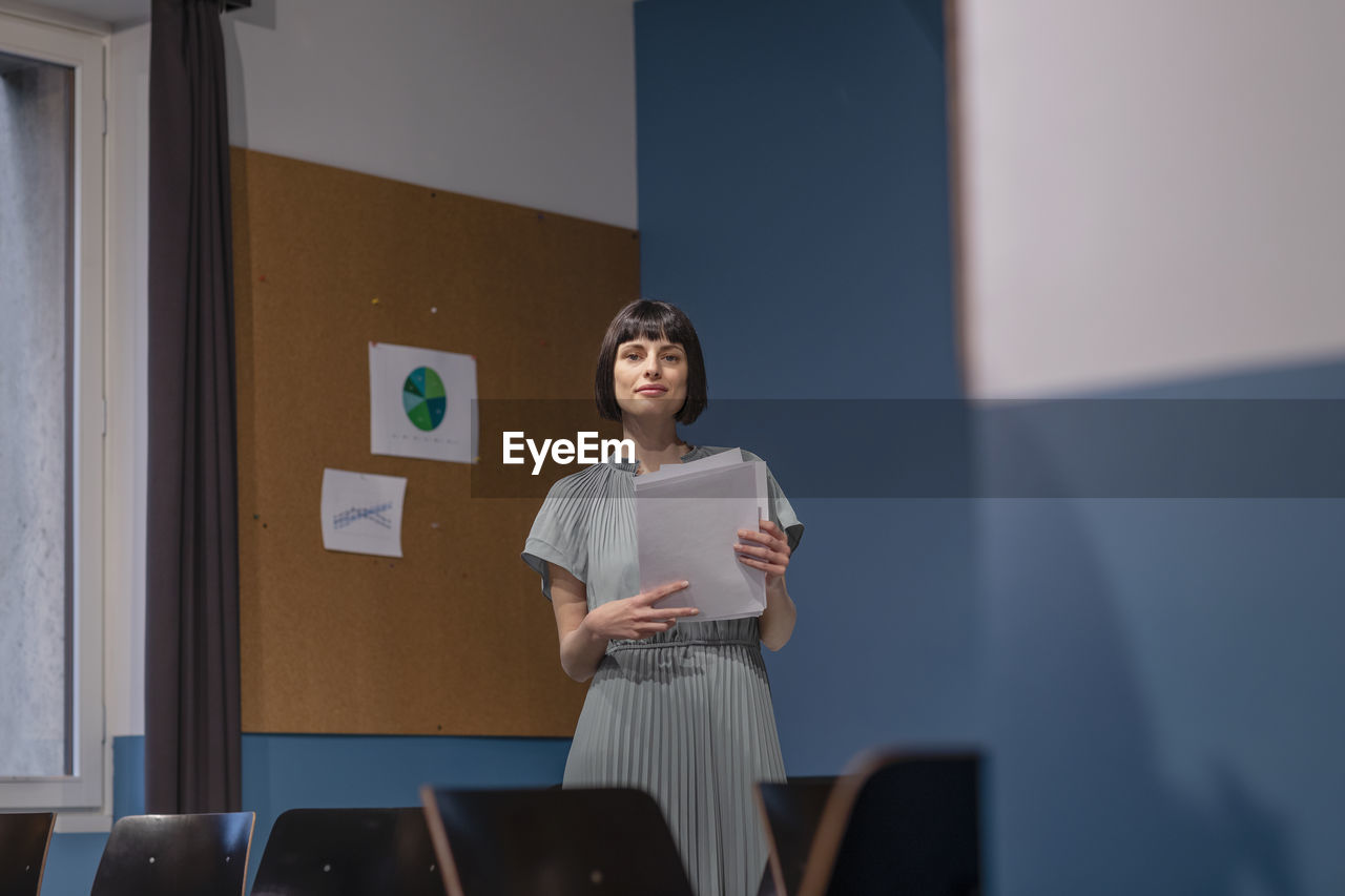 Confident businesswoman with documents in empty board room