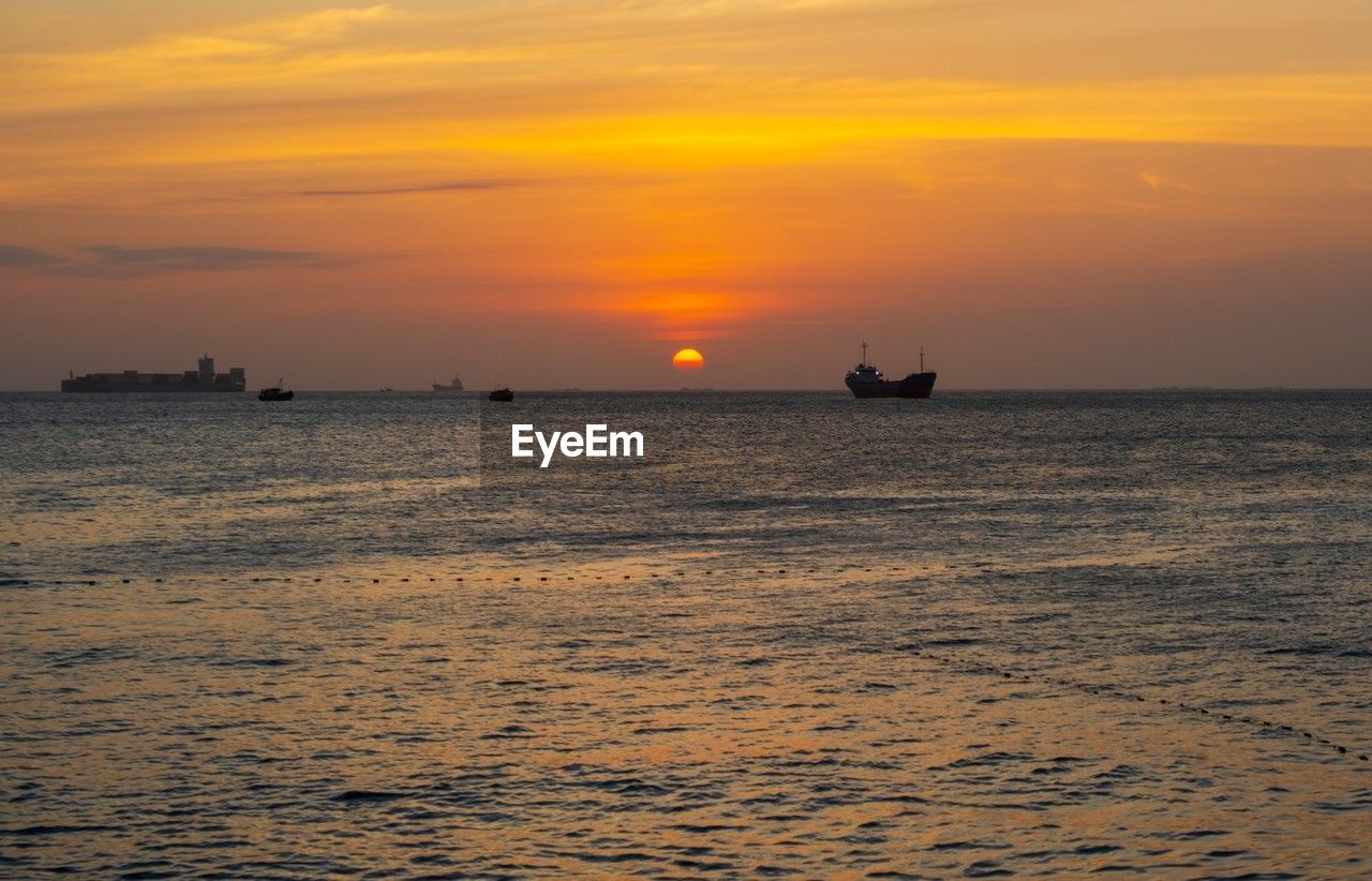 water, sea, sky, sunset, horizon, nautical vessel, transportation, ocean, beauty in nature, dawn, ship, shore, mode of transportation, scenics - nature, nature, cloud, horizon over water, orange color, coast, evening, tranquility, tranquil scene, afterglow, silhouette, wave, sailing, travel, no people, sun, outdoors, idyllic, beach, body of water, vehicle, seascape, land, dramatic sky, travel destinations, sunlight, waterfront