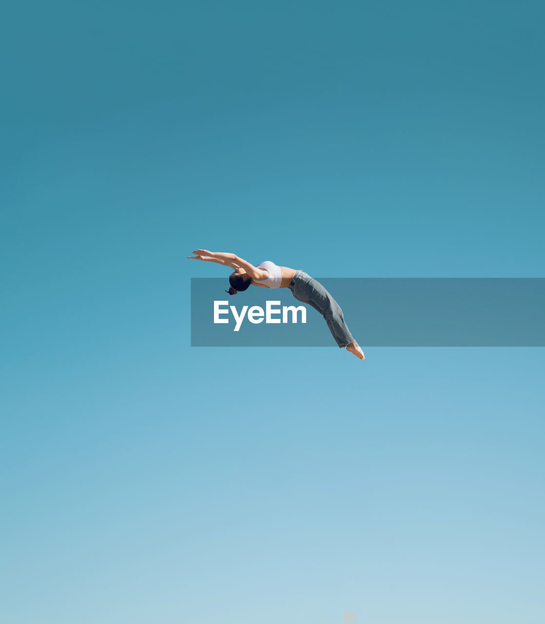 Full body side view of faceless female acrobat performing somersault high in air against clear cloudless blue sky on summer day