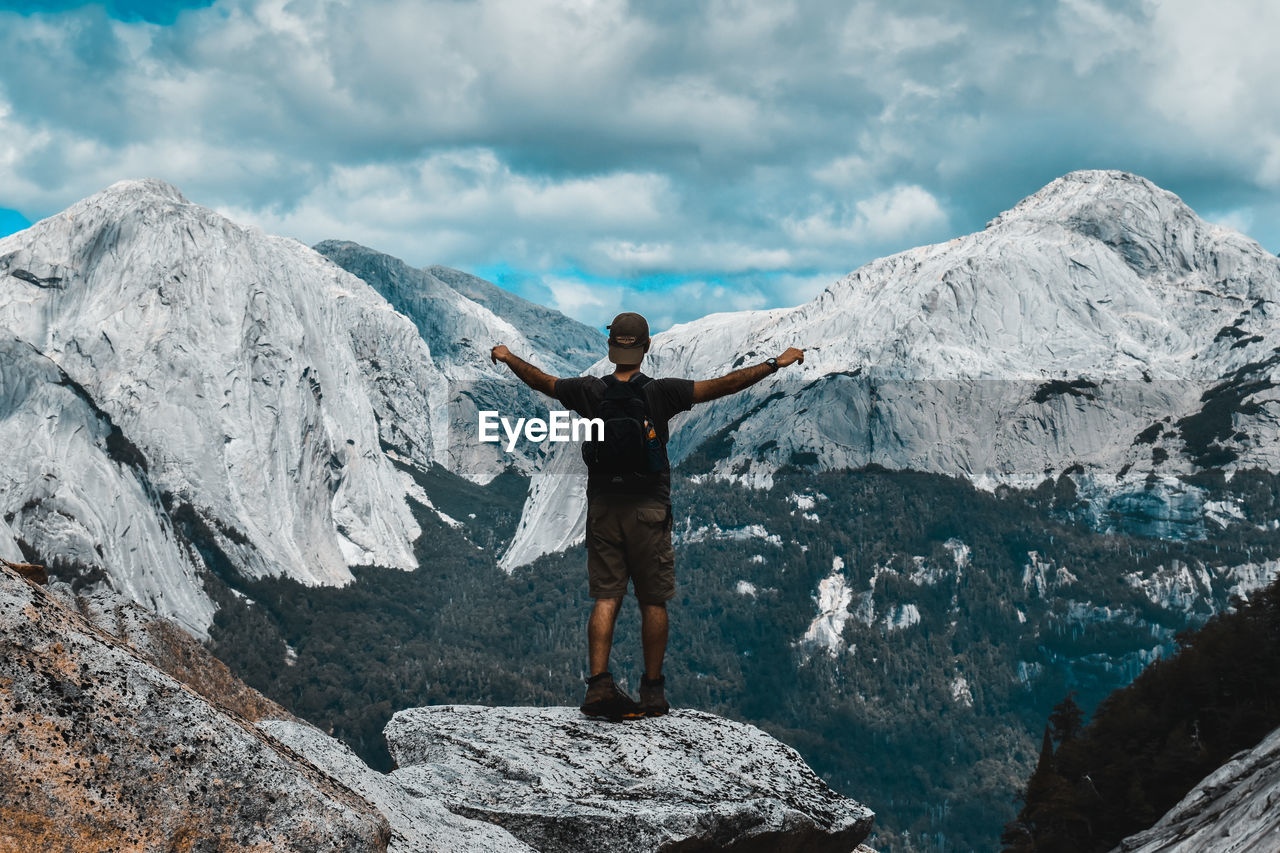 Rear view of man with arms outstretched standing on rock against mountains