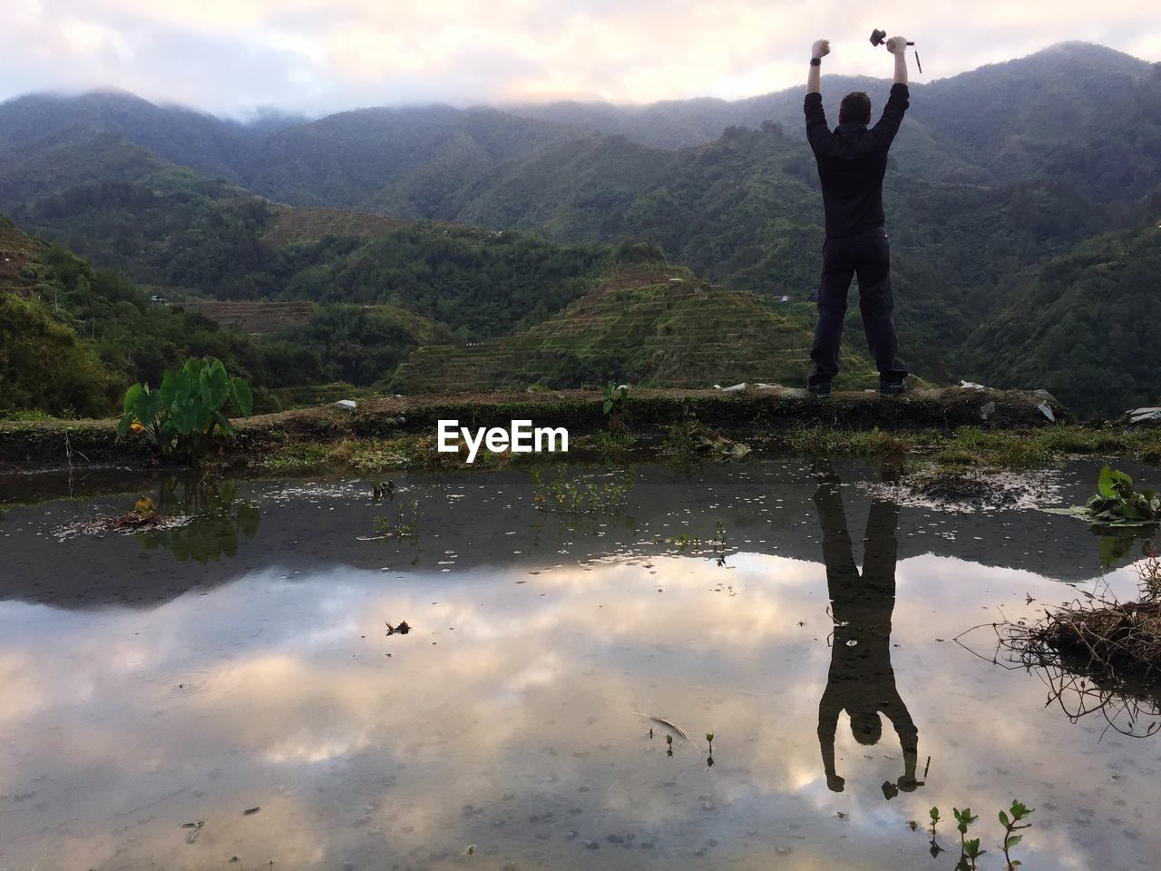 REAR VIEW OF MAN WITH REFLECTION IN LAKE AGAINST MOUNTAIN