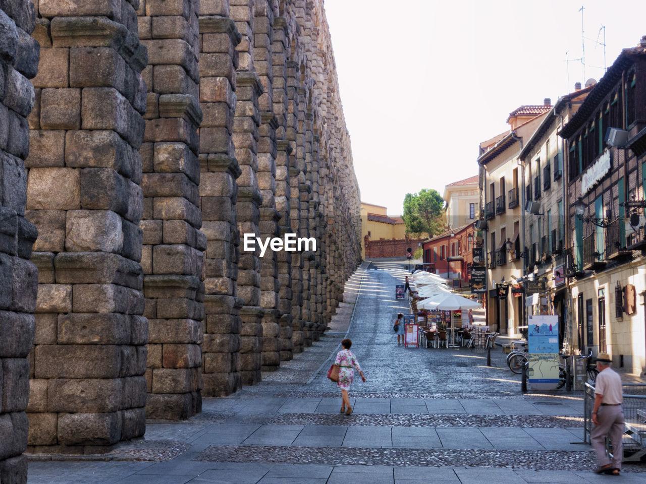 Woman walking on cobblestone street against clear sky in the segovia aqueduct 