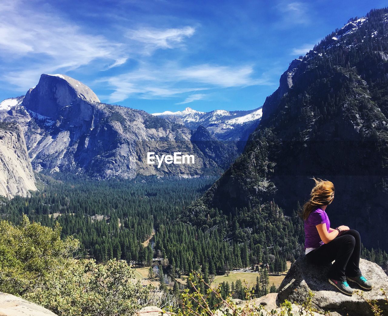 SIDE VIEW OF WOMAN SITTING ON ROCK AGAINST SKY