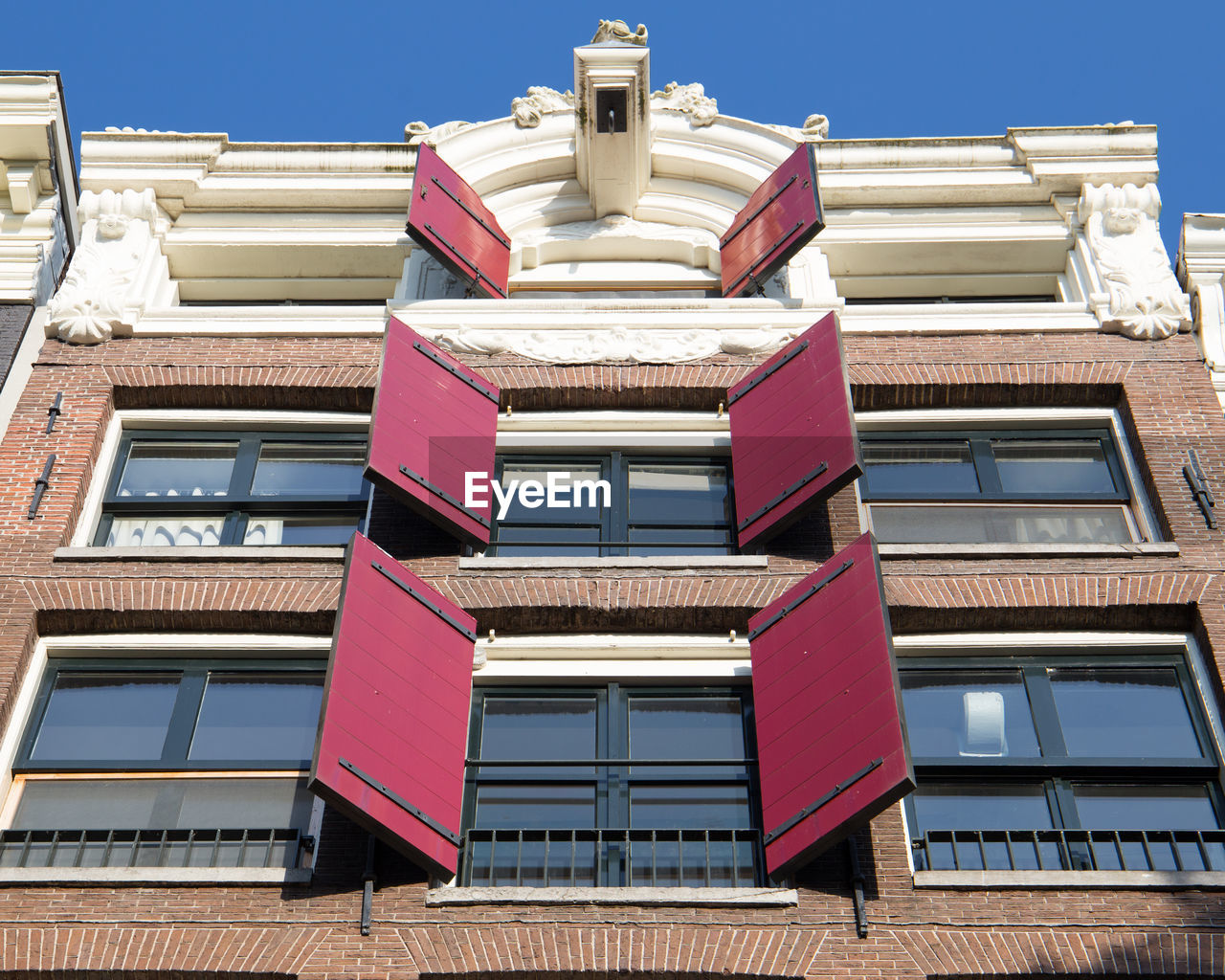 Low angle view of red shutters on a canal house in amsterdam against blue sky