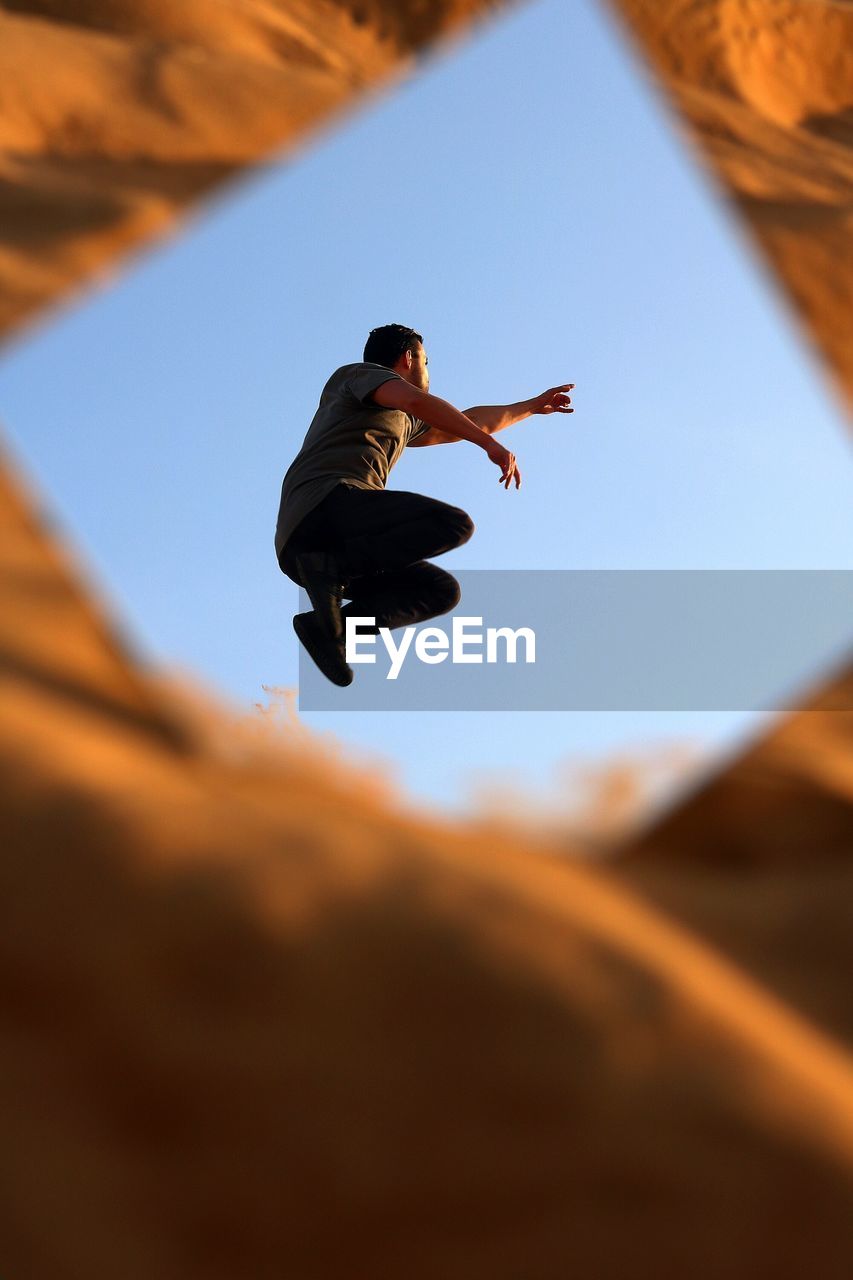 Reflection of man jumping in mirror against sky