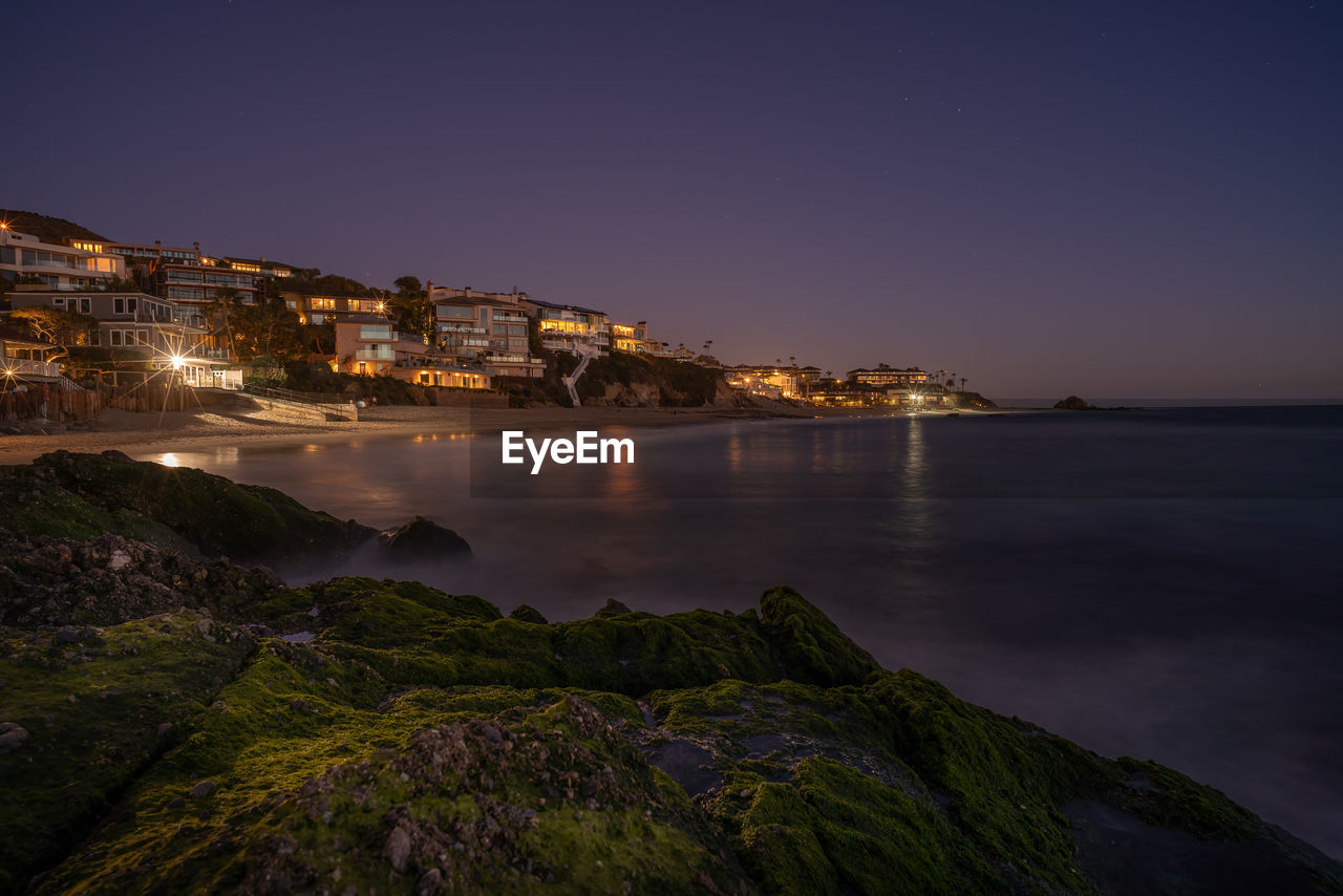 Illuminated buildings by sea against sky at night