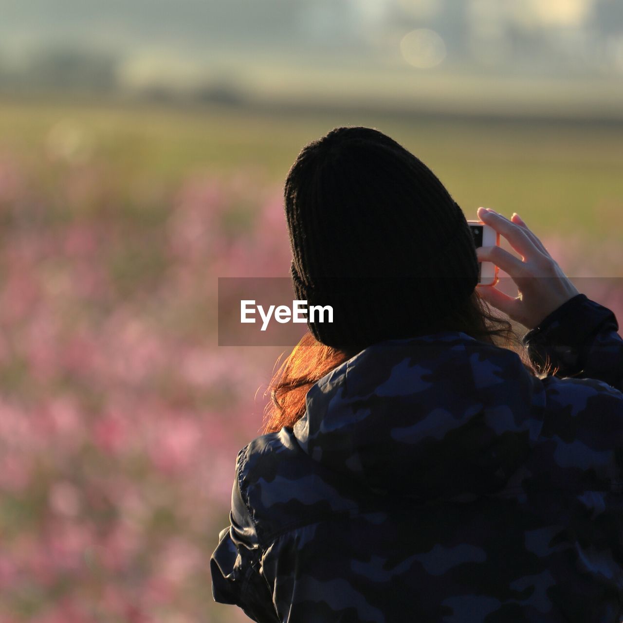 Rear view of woman photographing with mobile phone on field