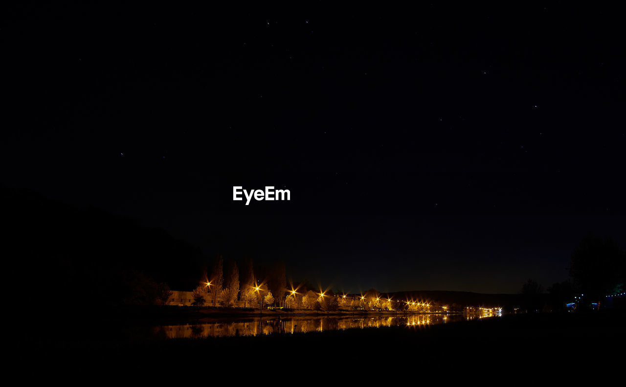 Illuminated trees by moselle river against sky at night