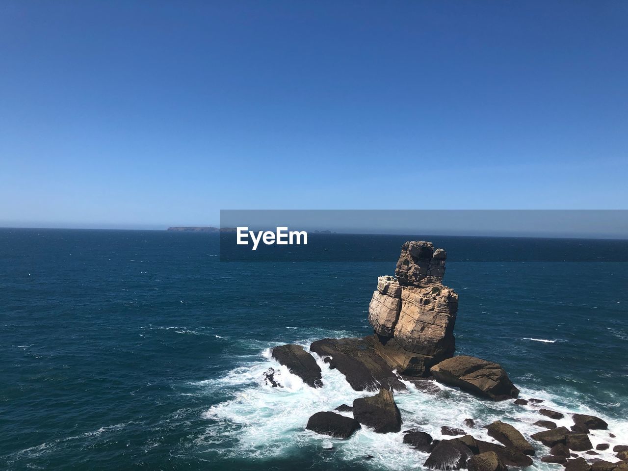 Rock formation in sea against clear blue sky