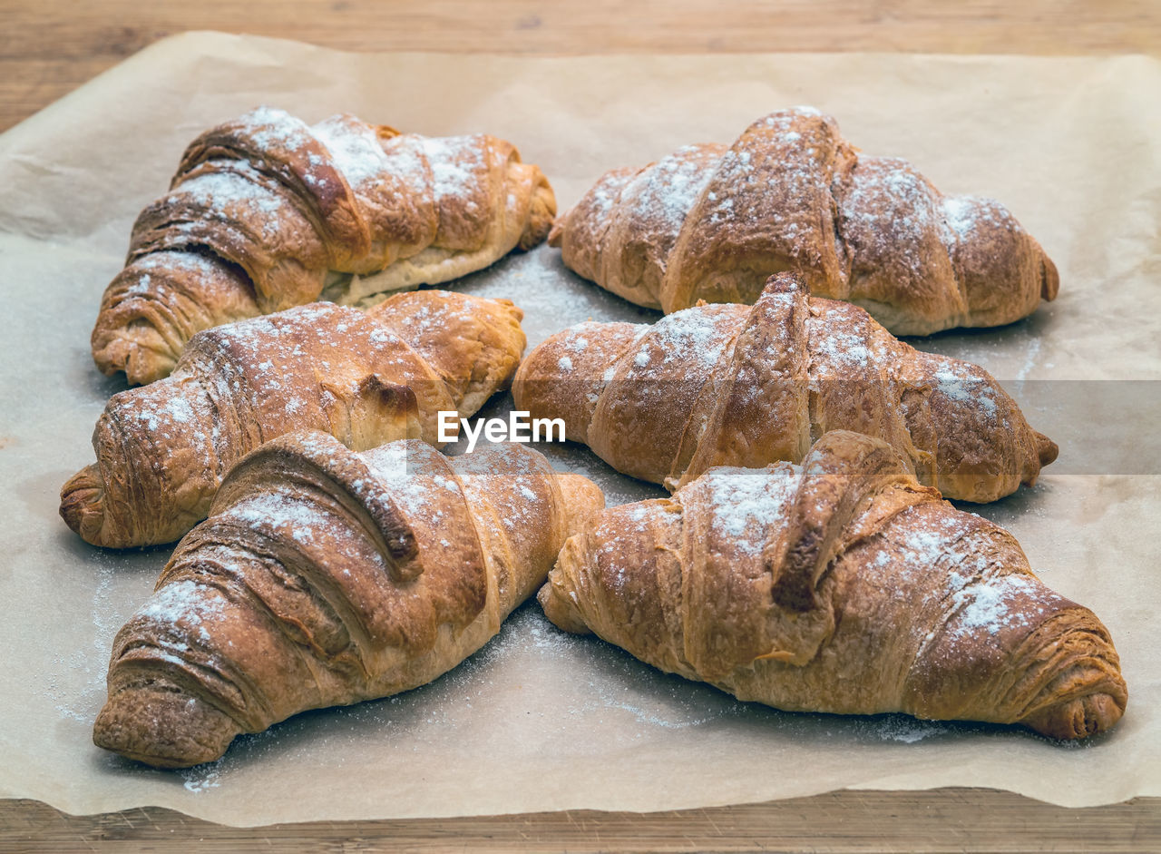 Freshly baked homemade croissants on baking paper sprinkled with powdered sugar.