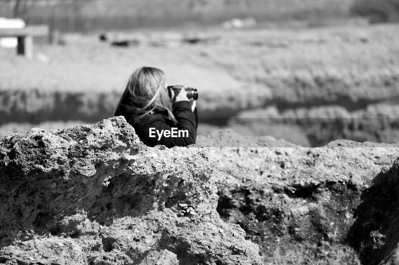 Side view of woman photographing amidst rocks at shore