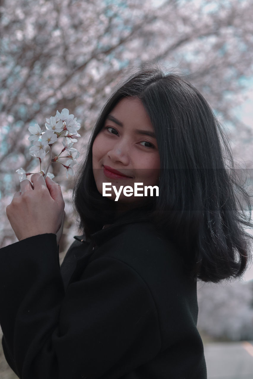 Portrait of smiling young woman standing by flowering plants