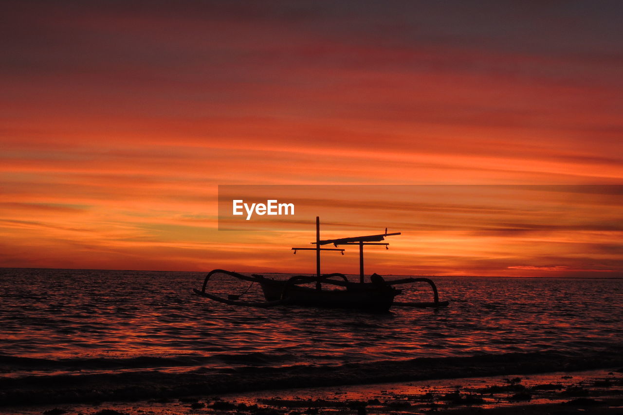 Silhouette boat in sea against orange sky