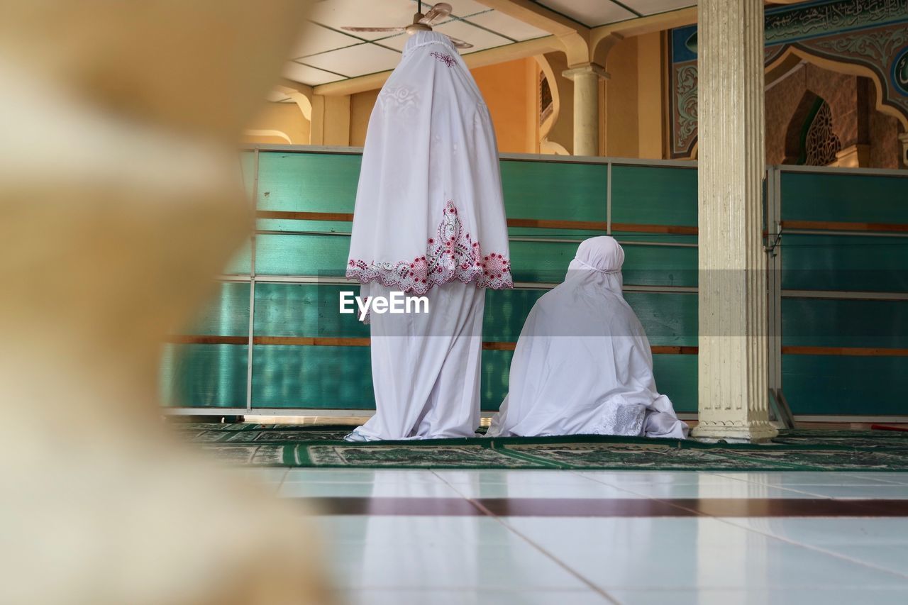 Rear view of women wearing traditional dress praying in mosque