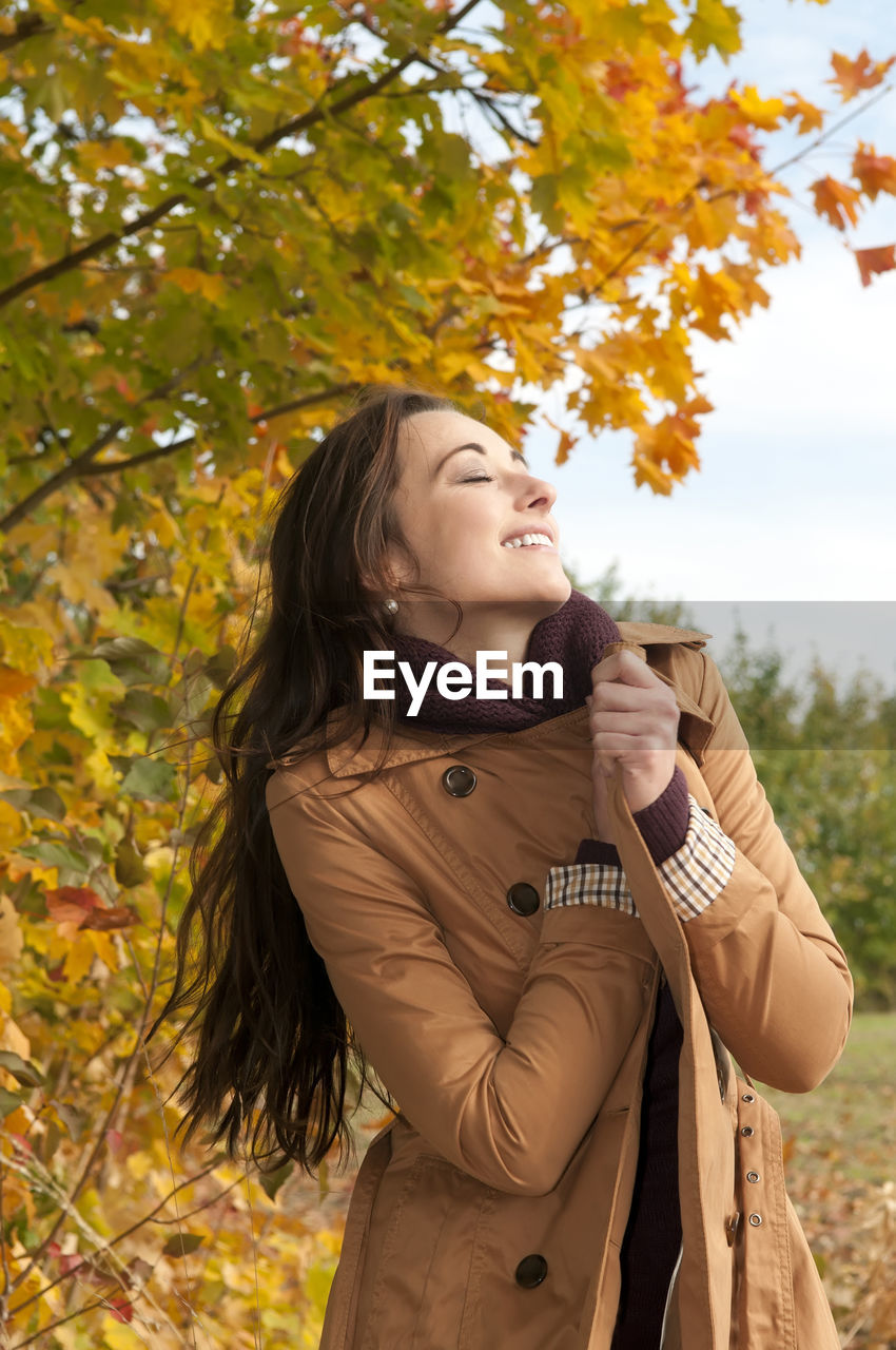 Woman wearing coat standing against trees in park during autumn