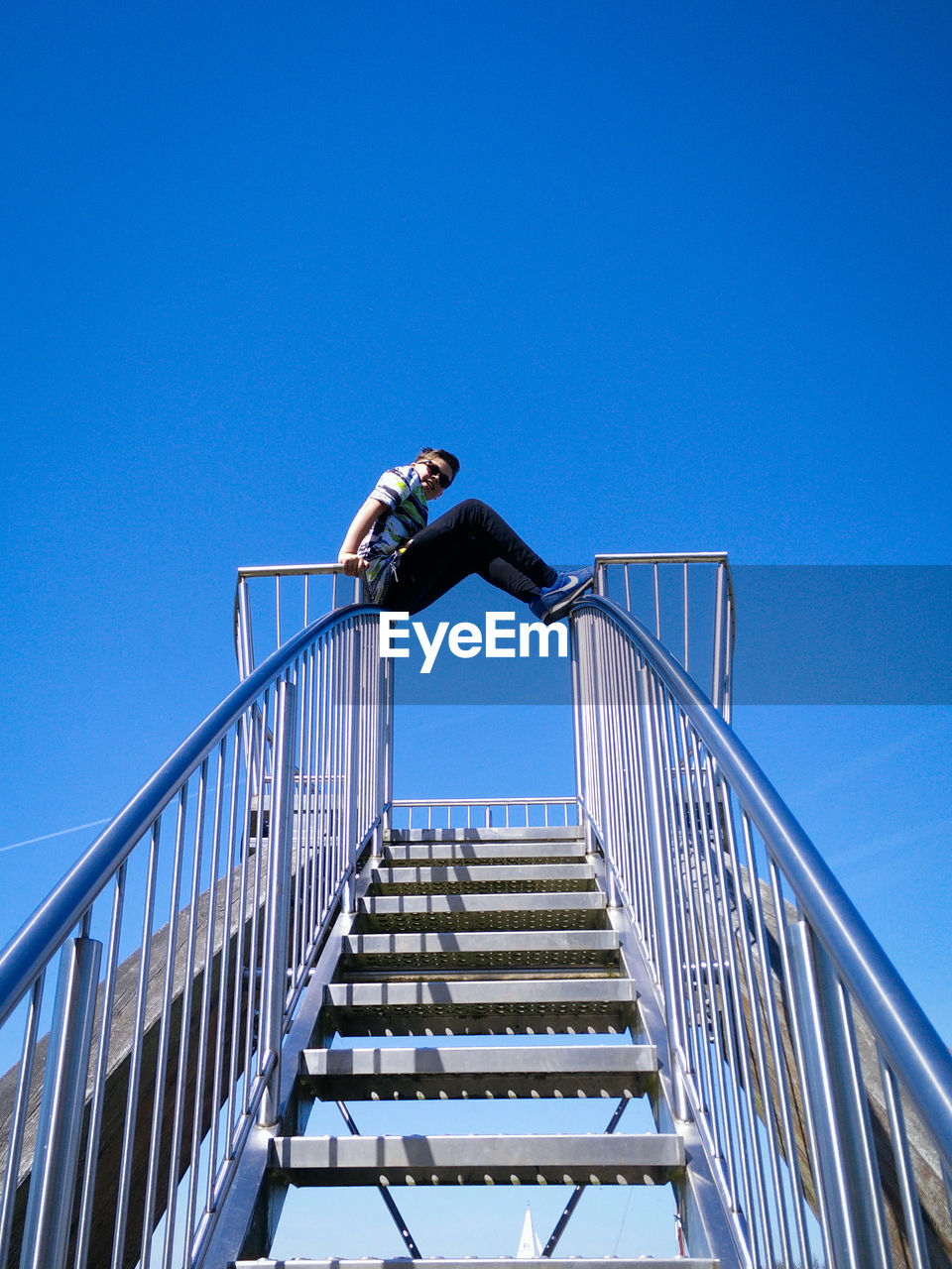 Low angle view of man on steps against clear blue sky