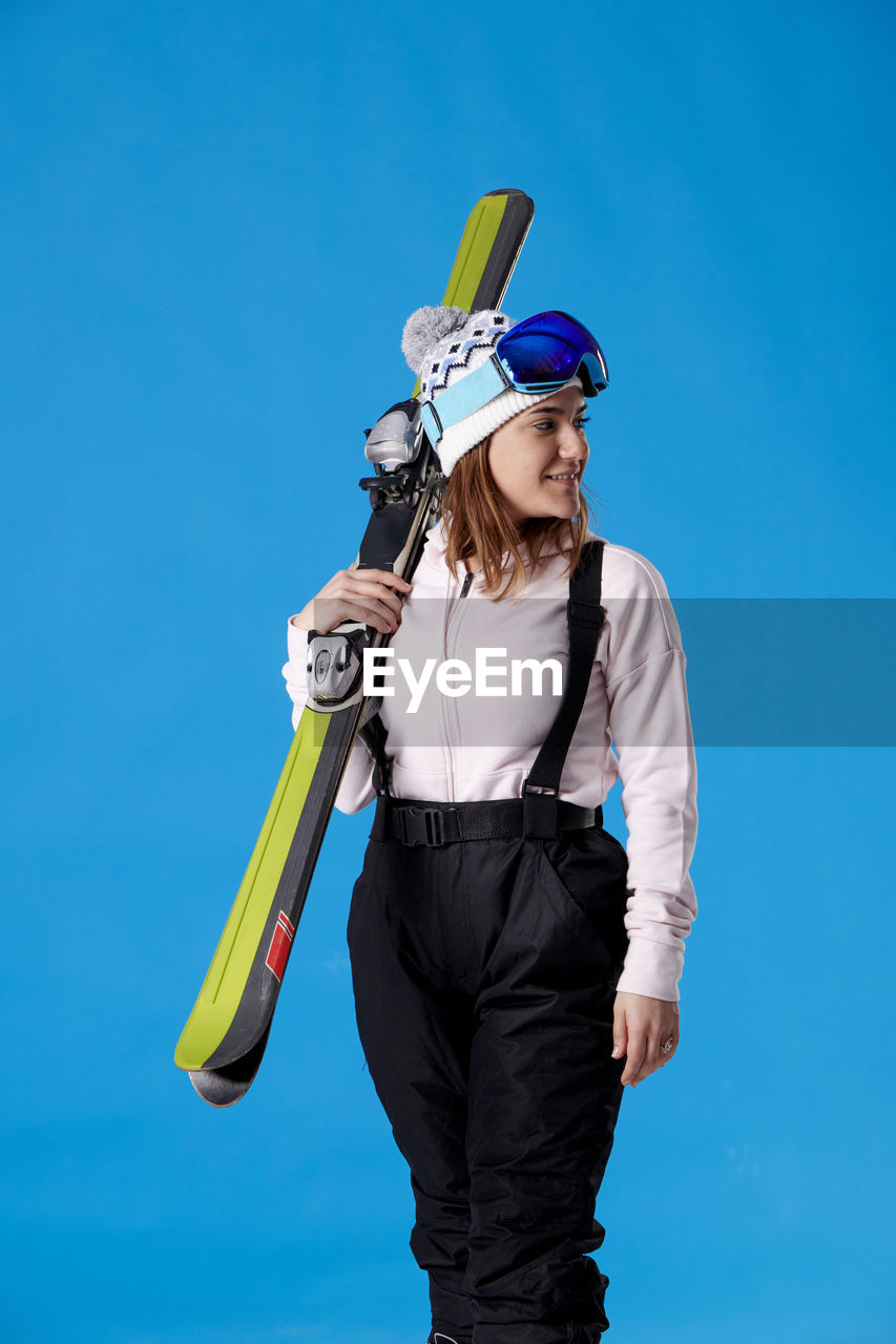 one person, blue, adult, sports, women, young adult, clothing, nature, skiing, sky, holding, extreme sports, standing, leisure activity, colored background, copy space, emotion, portrait, front view, day, female, fun, three quarter length, adventure, happiness, sports equipment
