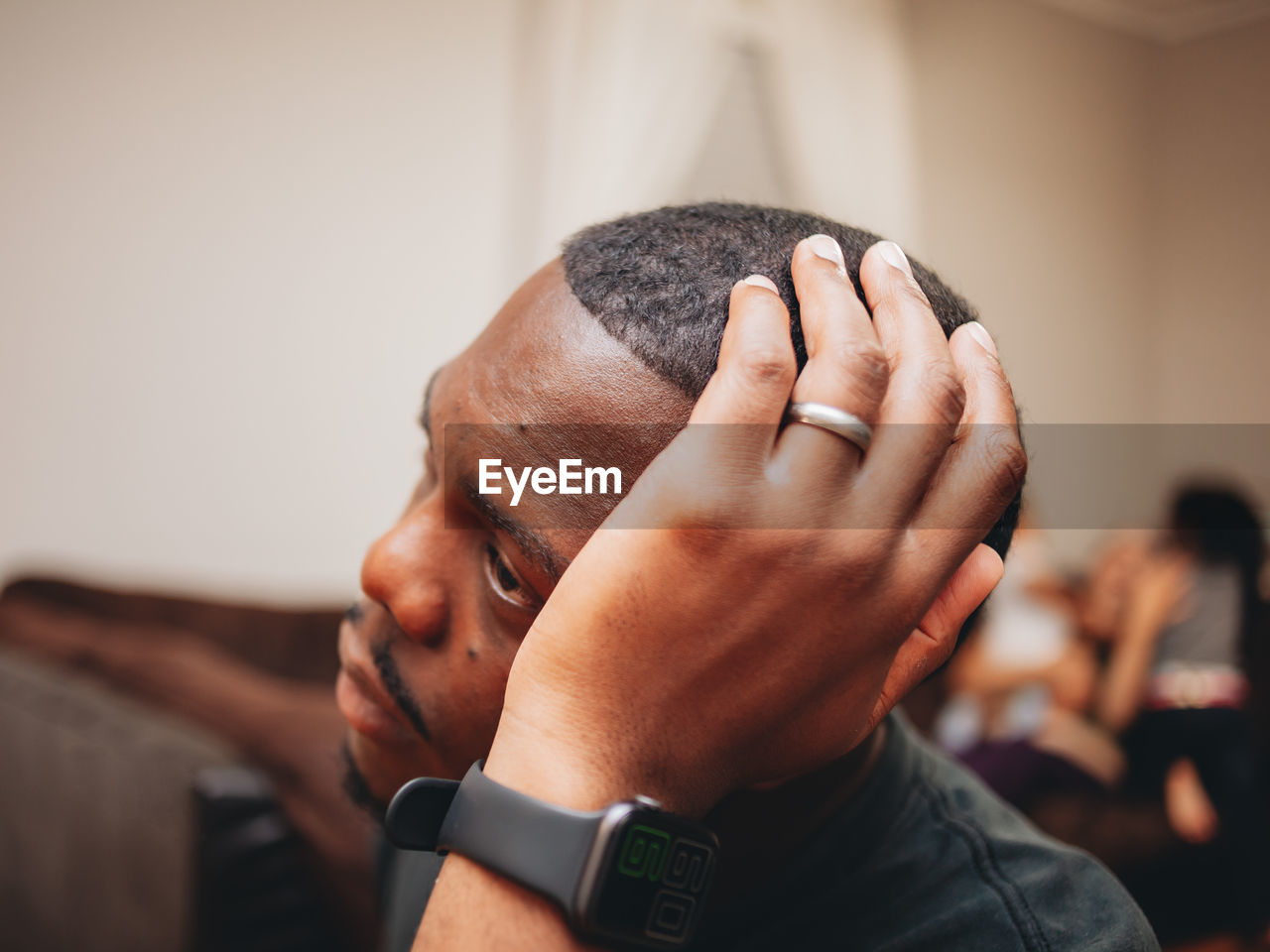 Black man at home looking sad and depressed while mother plays with kids in the background