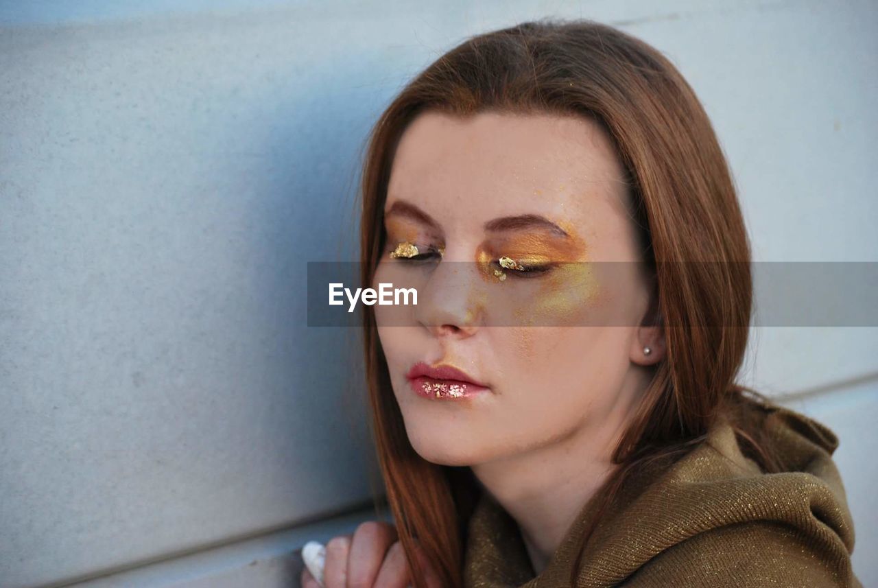 Close-up of young woman with make-up against wall